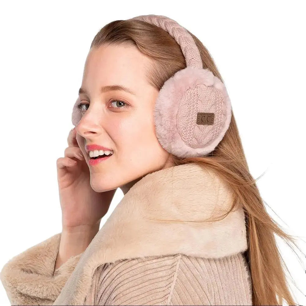 A woman wearing fluffy light pink earmuffs and a beige faux-fur collar jacket, shown from the side against a plain white background.