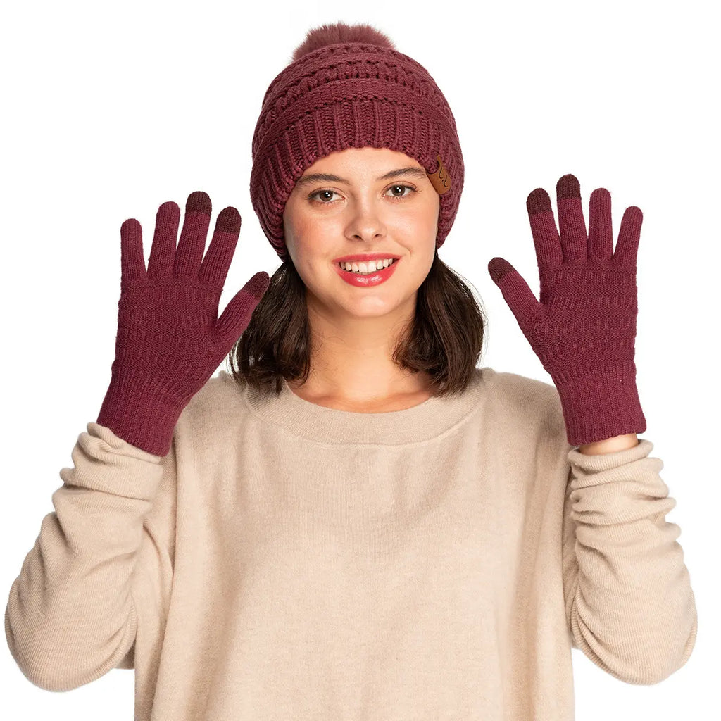 A woman wearing a matching knit beanie with a pom-pom and matching knit touchscreen-compatible gloves, posed against a solid white background.