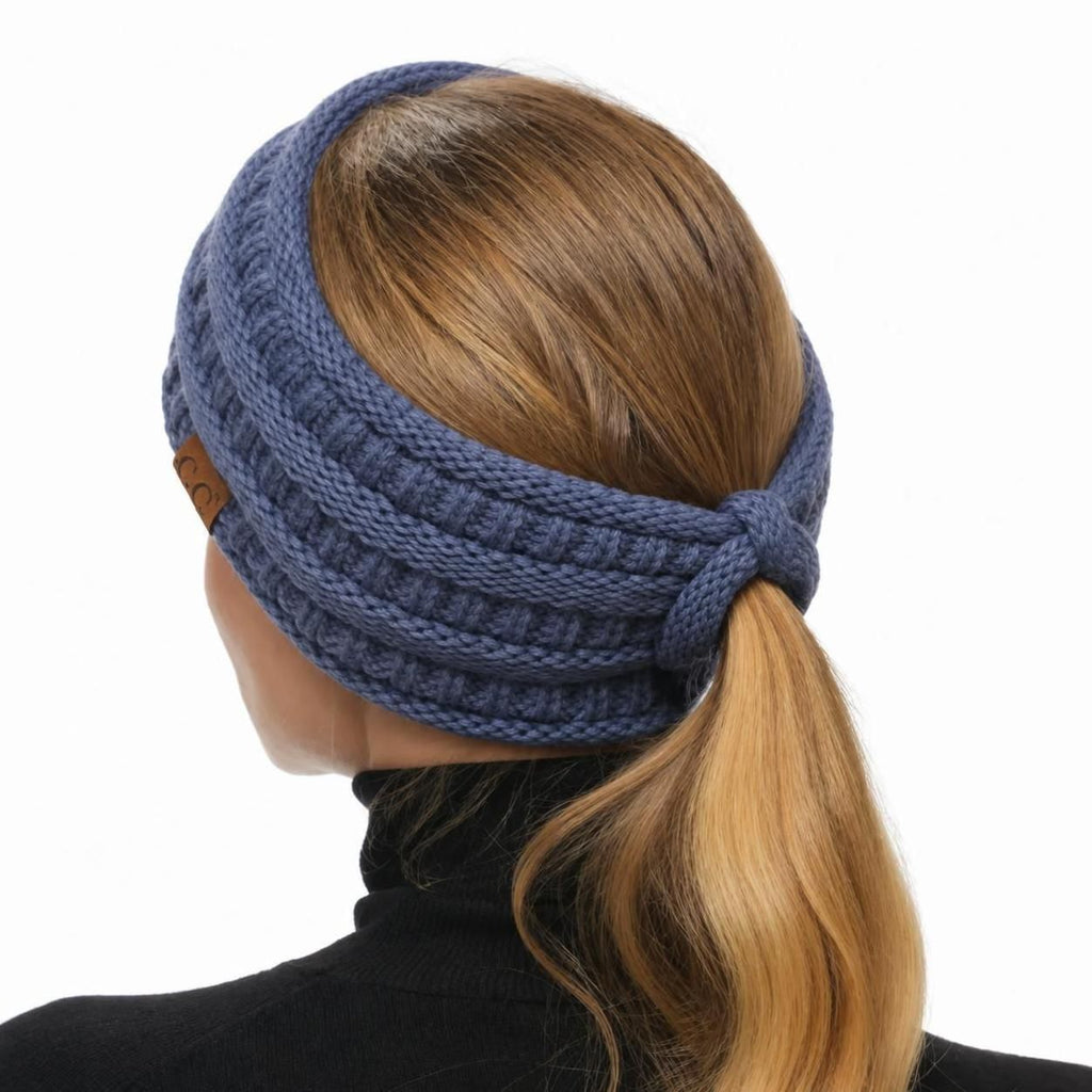 A woman shown from the back wearing a ribbed knit ear warmer headband in a dusty blue color, holding her blonde ponytail against a plain white background.