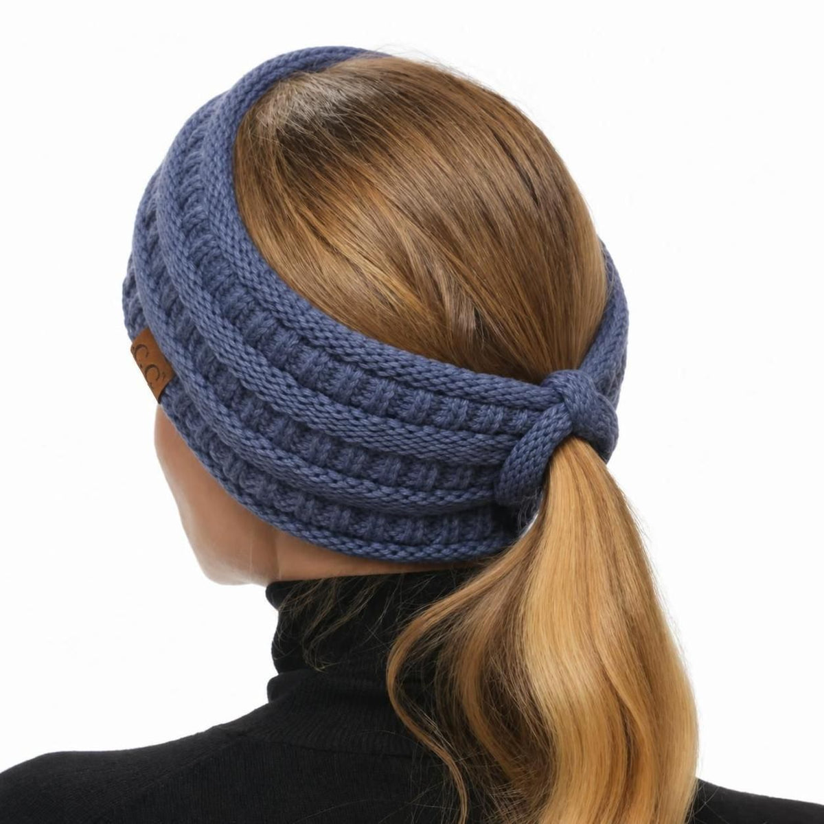 A woman shown from the back wearing a ribbed knit ear warmer headband in a dusty blue color, holding her blonde ponytail against a plain white background.