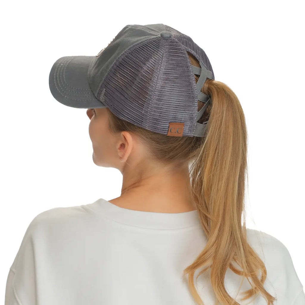A woman shown from the back wearing a gray trucker-style cap with a mesh back and a brown leather brand patch on the side, against a plain white background.